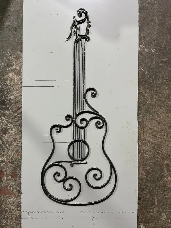 Gitarrformat metallföremål med strängar och spiraler, lagt på en plåt.